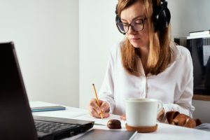 Remote work. Online courses, distance education and e-learning concept. Woman in headphones listen audio course at laptop and makes notes in notebook
