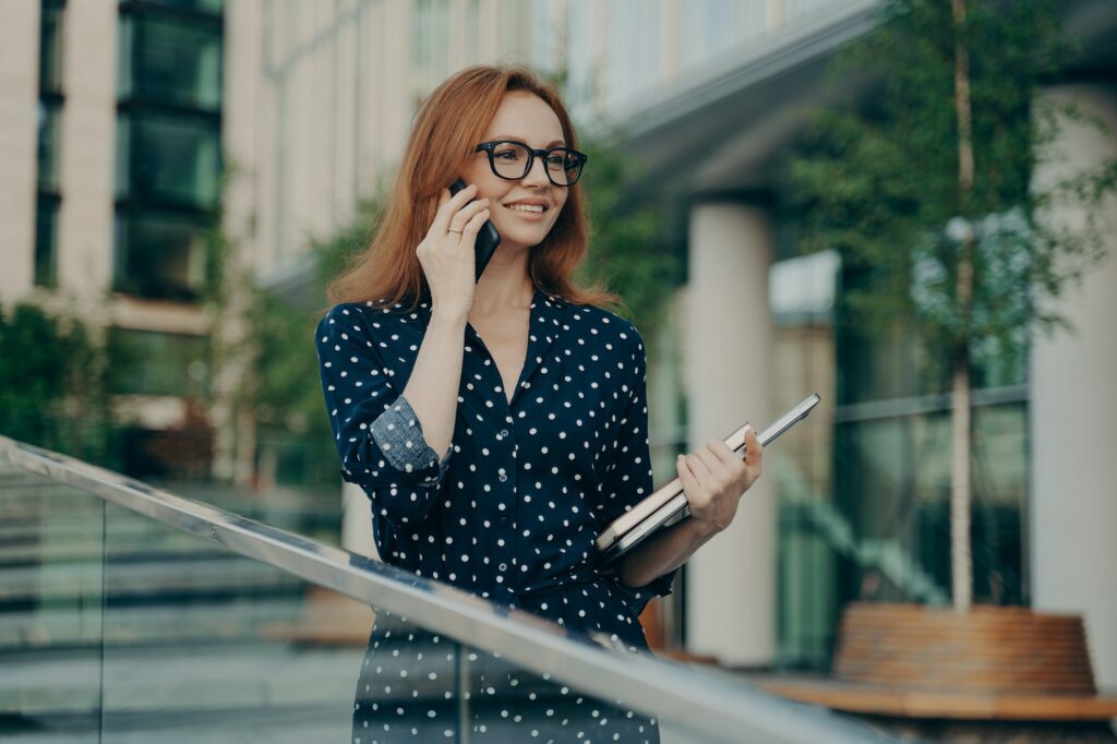 Satisfied female consultant with red hair makes consultancy call on smartphone