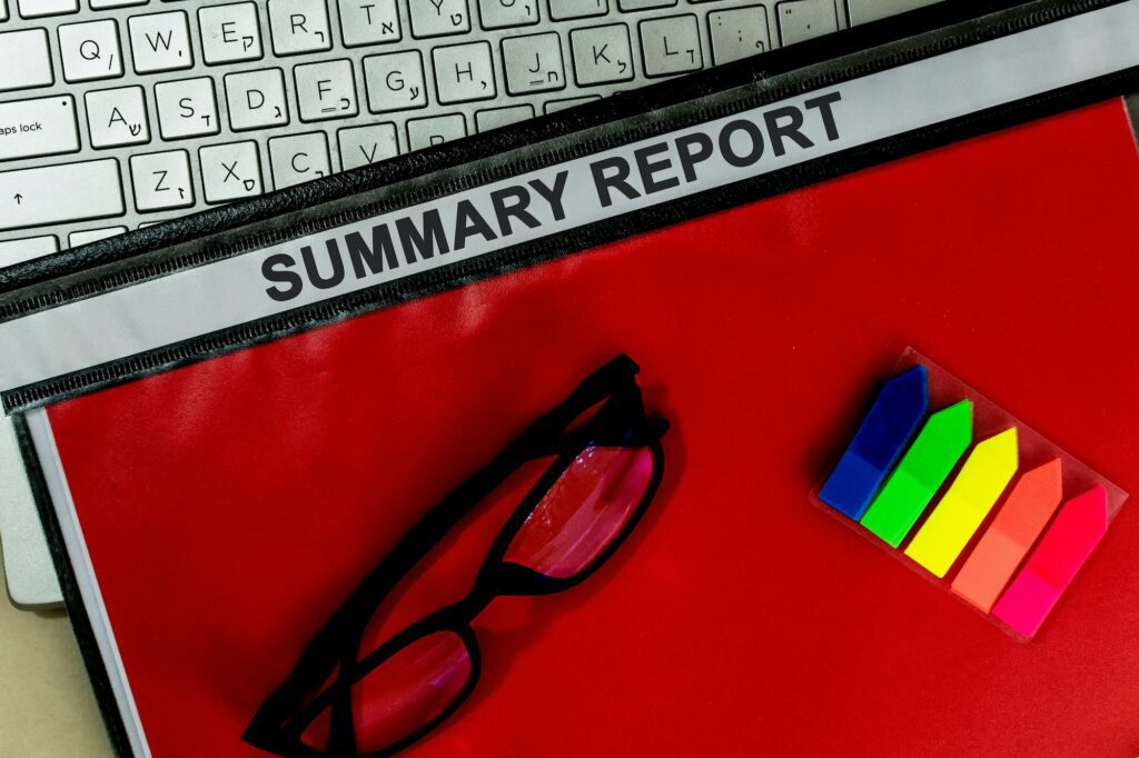 Top view of glasses on a red folder labelled "SUMMARY REPORT" on a laptop in the office